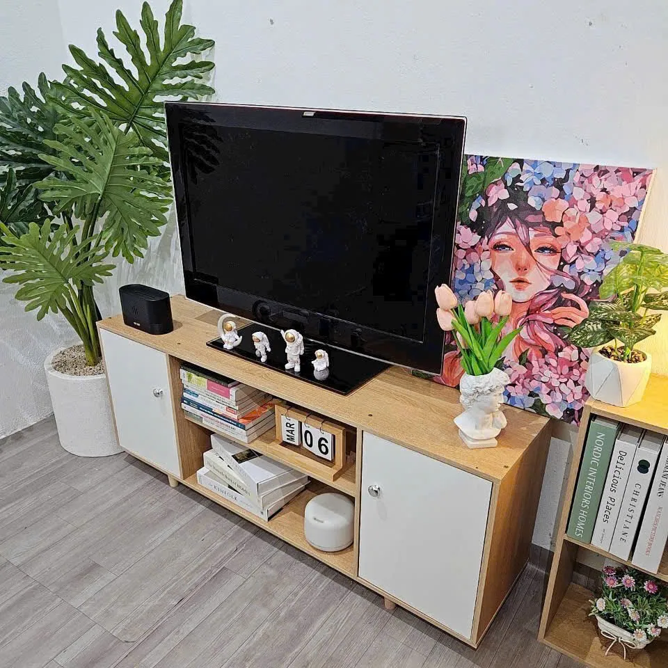Kệ tivi gỗ 2 cánh màu trắng, có các ngăn chứa sách, đồ trang trí và mặt trên bày TV cùng tượng nhỏ, phù hợp cho nội thất hiện đại