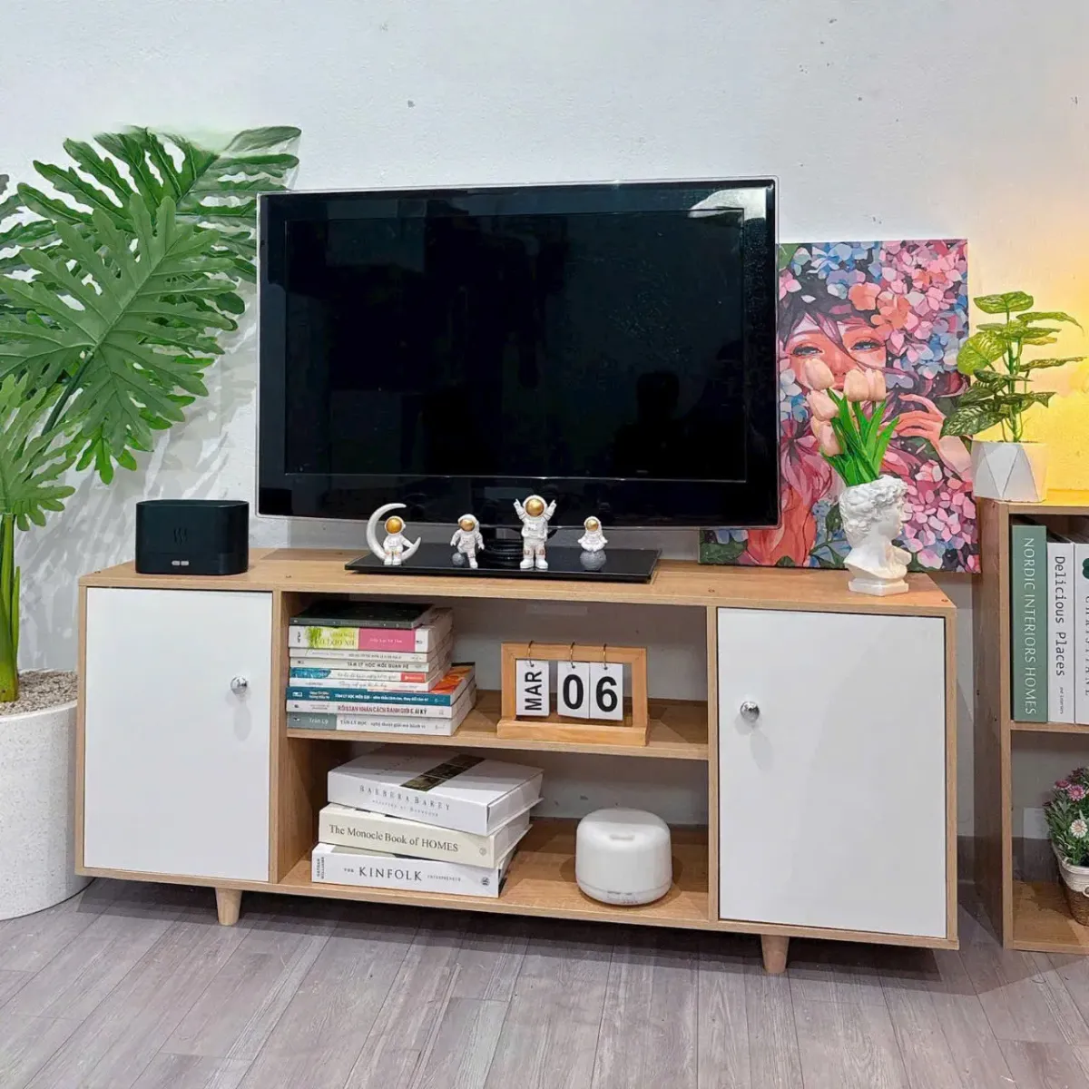 Kệ tivi gỗ 2 cánh màu trắng, có các ngăn chứa sách, đồ trang trí và mặt trên bày TV cùng tượng nhỏ, phù hợp cho nội thất hiện đại