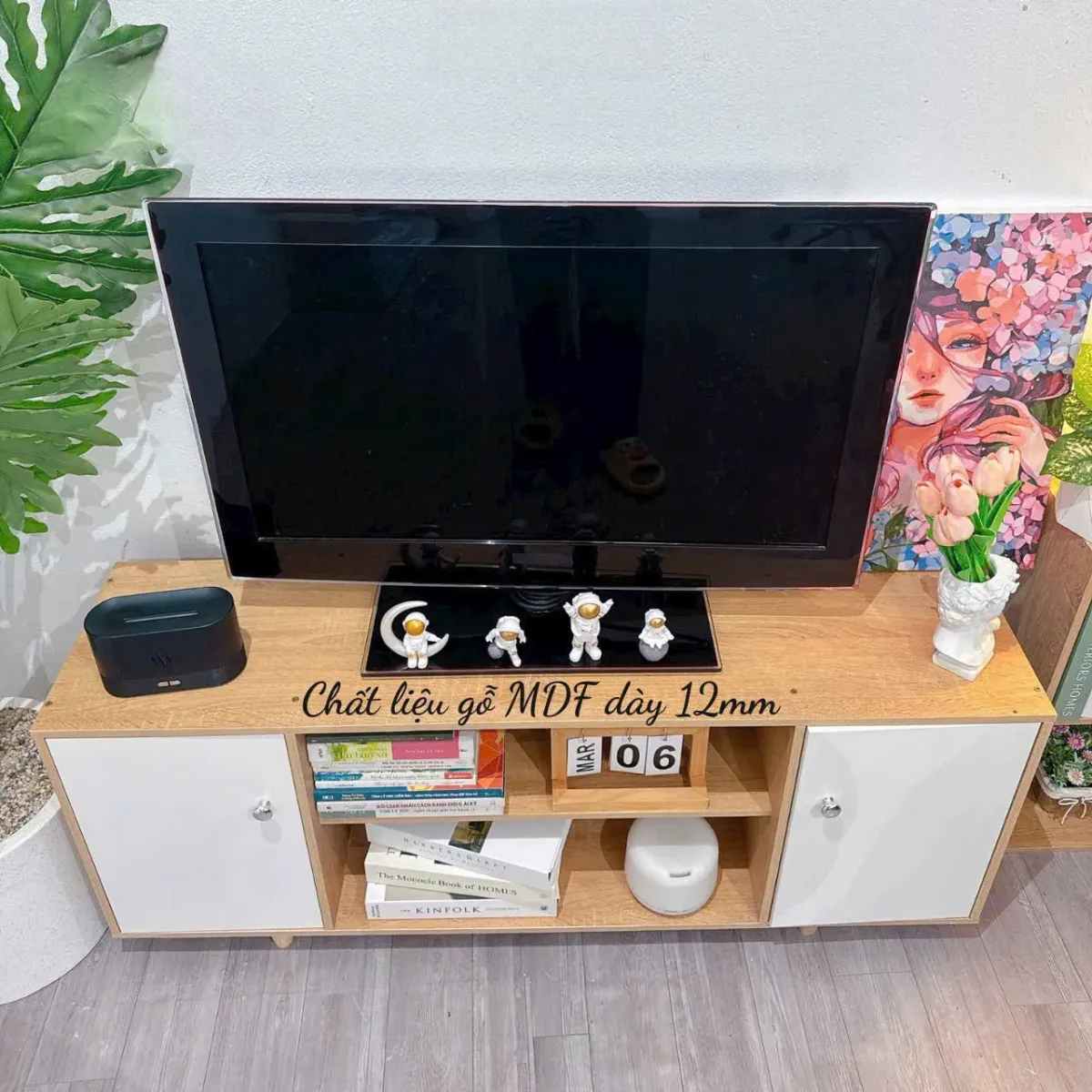Kệ tivi gỗ 2 cánh màu trắng, có các ngăn chứa sách, đồ trang trí và mặt trên bày TV cùng tượng nhỏ, phù hợp cho nội thất hiện đại
