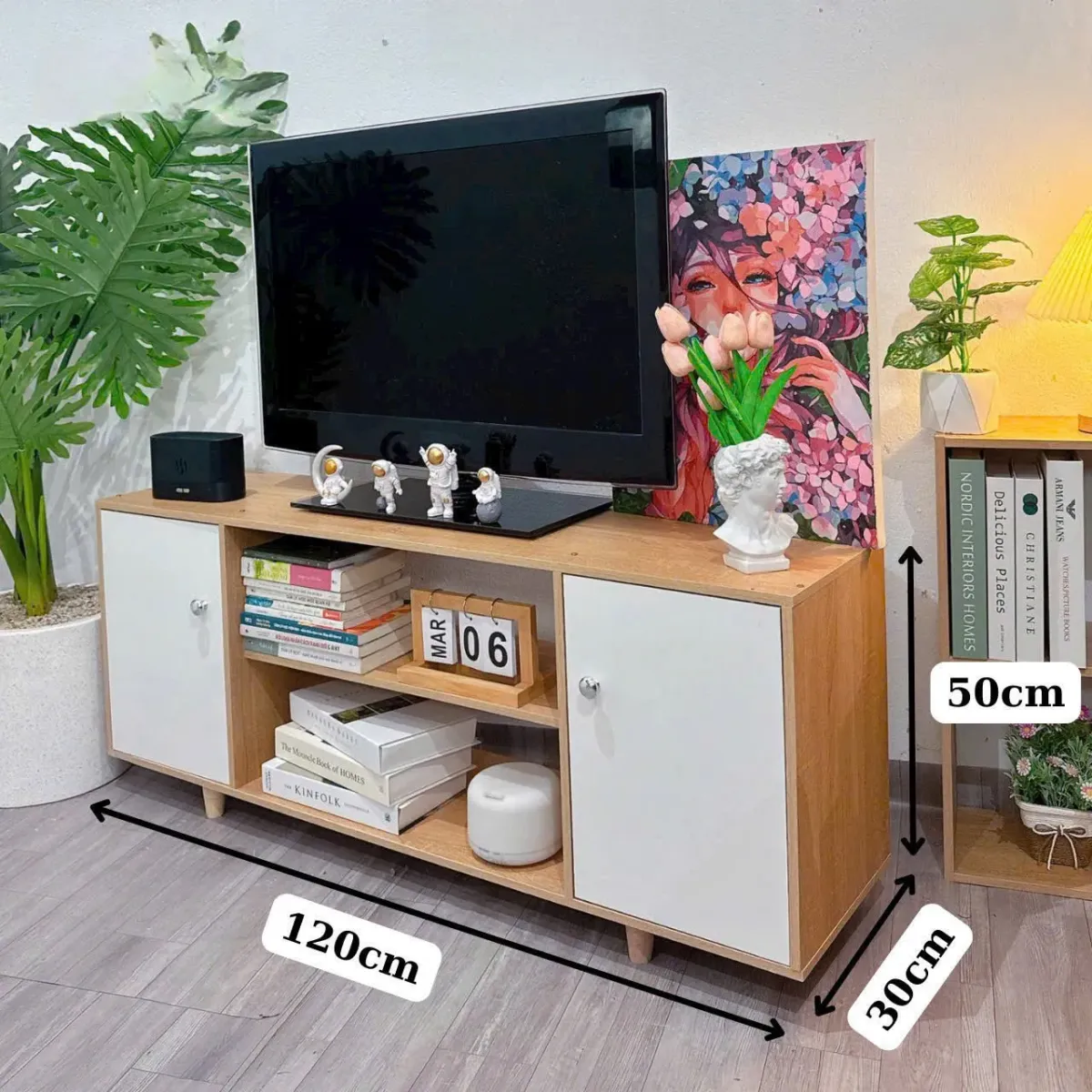 Kệ tivi gỗ 2 cánh màu trắng, có các ngăn chứa sách, đồ trang trí và mặt trên bày TV cùng tượng nhỏ, phù hợp cho nội thất hiện đại