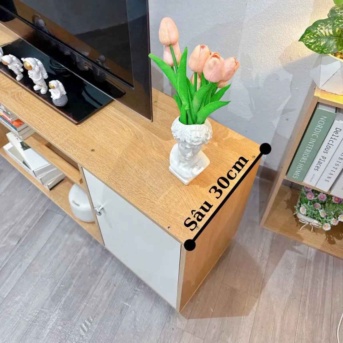 Kệ tivi gỗ 2 cánh màu trắng, có các ngăn chứa sách, đồ trang trí và mặt trên bày TV cùng tượng nhỏ, phù hợp cho nội thất hiện đại