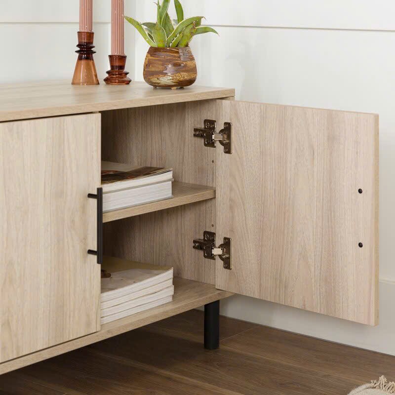 Kệ tivi làm từ gỗ công nghiệp, có 2 ngăn kéo và 2 cánh mở, thiết kế hiện đại, màu vân gỗ sáng, chân cao đen, phù hợp phòng khách tối giản.